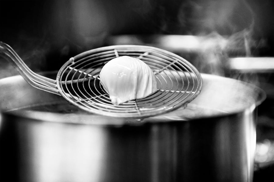 Espumadera con un alimento blanco sobre una olla humeante en la cocina de Actual Catering