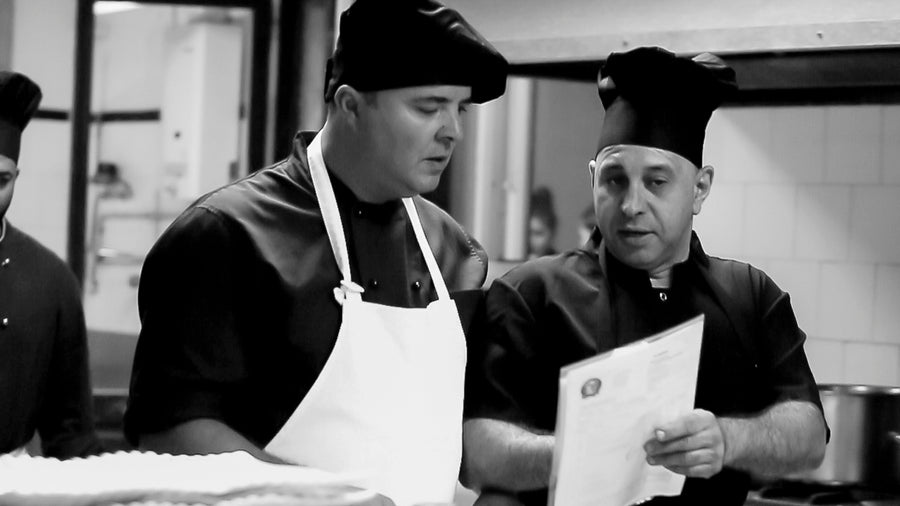 Dos cocineros con gorro revisando una hoja de pedido en la cocina de Actual Catering