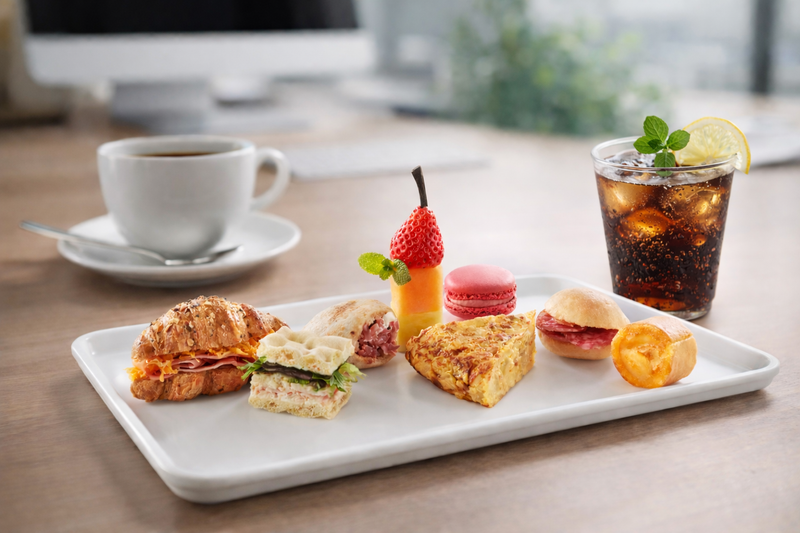 Bandeja de coffee break con mini croissant, bocadillos, tortilla, macarons y brocheta de fruta, junto a un café y un refresco